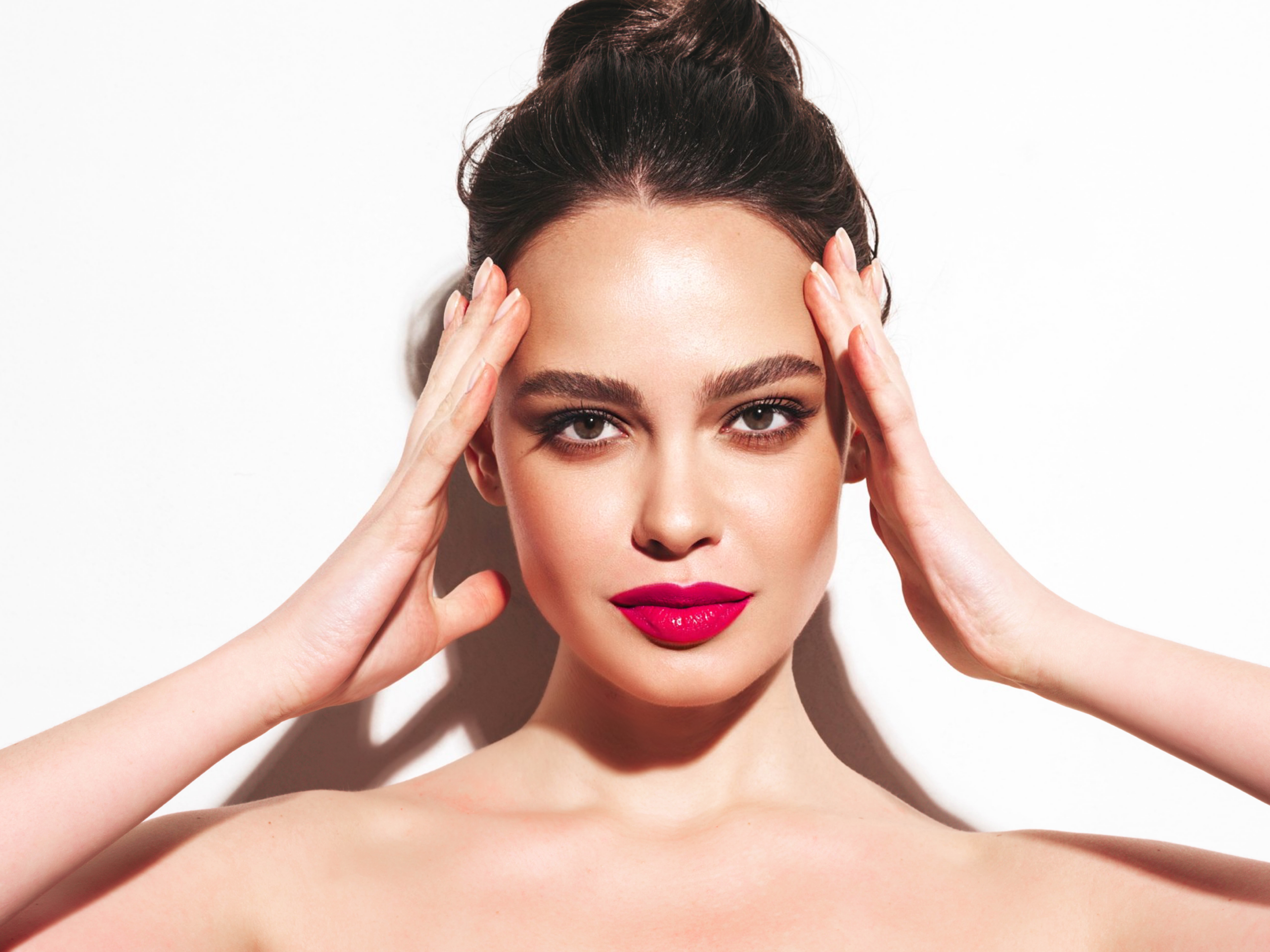 Fashion beauty portrait of young brunette woman with evening stylish makeup and perfect clean skin. Sexy model with hair in a bun posing in studio. With pink bright natural lips. Isolated on white